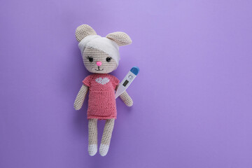 Canvas Print - Toy bunny with bandage and thermometer on violet background, top view with space for text. Children's hospital