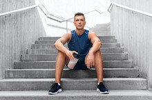 Fitness, Sport And People Concept - Tired Young Man With Protein Shake In Bottle Sitting On Stairs
