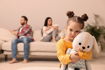 Wall Mural - Sad little girl with toy and her arguing parents on sofa in living room