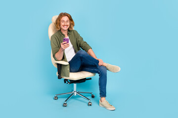 Sticker - Full length body size view of attractive cheerful guy sitting using device gadget smm app isolated over pastel blue color background