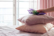 Female hand putting bunch of lavender on top of color pillows on bed. Professional maid prepares hotel room for guests by decorating bed with fresh flowers.