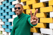 Happy Man Gesturing Peace Sign In Front Of Brick Wall