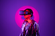 Spotlight Falling On Woman Wearing Virtual Reality Simulator Against Purple Background