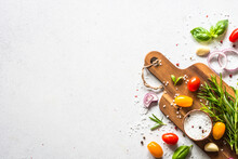 Food Cooking Background On White Stone Table. Fresh Vegetables, Herbs And Spices With Wooden Cutting Board. Ingredients For Cooking With Space For Text.