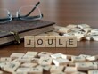 joule word or concept represented by wooden letter tiles on a wooden table with glasses and a book
