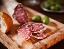 Salami Sliced On A Cutting Board With Bread; Bowl Of Green Olives In The Background.