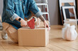 © Mediaphotos - Horizontal shot of unrecognizable young woman sitting on floor getting ready for moving to new house packing things into boxes and taping them
