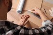 © New Africa - Man using utility knife to open parcel at wooden table, closeup