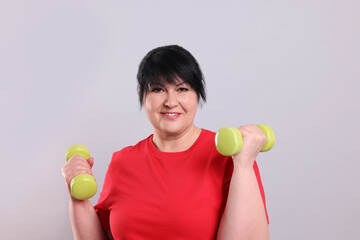 Canvas Print - Happy overweight mature woman doing exercise with dumbbells on grey background