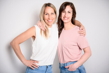 Wall Mural - Two smiling best girl friends blond and brunette on white background. Closeup face portrait of two young beautiful women.