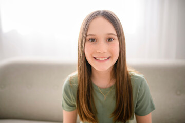 smiling young girl sit on sofa looking at camera