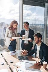 Wall Mural - Smiling businessmen drink coffee and discussing documents with graphs and charts in a modern office during meeting. Teamwork concept