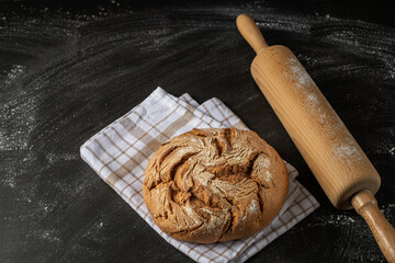 Wall Mural - Fresh baked rye wheat loaf of bread  closeup on linen towel with wooden rolling pin on flour background with copy space.