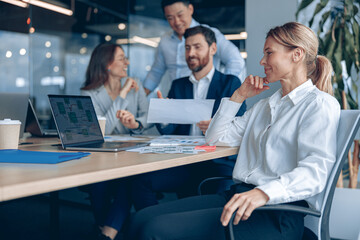 Wall Mural - smiling confident female boss sitting on meeting and looking at side with her colleagues at backgrou