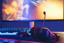 Close Up Of Headset Laying On Gaming Desktop. Selective Focus. Monitor And Keyboard On Background. Professional Gaming Setup In Neon Lights Ready To Use For Online Esport Competition. Cyber Sport