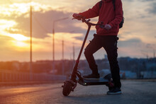 A Man Rides Around The City On A Powerful Electric Scooter. Road And Sunset On The Background