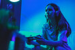 © Alberto - involved gamer girl playing video games on the console at home with blue neon lights