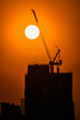 Leinwandbild Motiv Silhouette of a construction crane on a building with an orange sun on the background