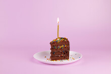 Slice Of Birthday Cake With Candle And Colorful Sprinkles On Pink Background. Chocolate Cake Slice, Birthday Party Minimal Concept.
