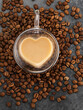 Glass cup in form of heart with coffee on coffee beans background.