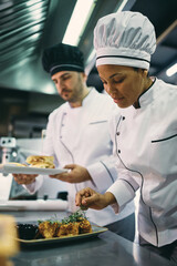 Wall Mural - African American professional cook serving dish with her coworker in restaurant.