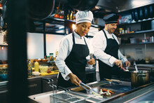 Two Professional Cooks Preparing Meal In Kitchen At Restaurant.