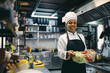 © Drazen - Black female chef preparing food in kitchen at restaurant and looking at camera.