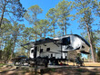 A fifth wheel trailer and campsite in the woods.