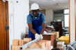 © JackF - African-american man construction worker standing at brick stack and carrying metal plank in building site.