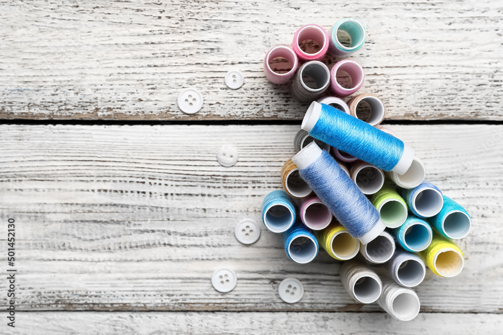 Sewing threads and buttons on light wooden background