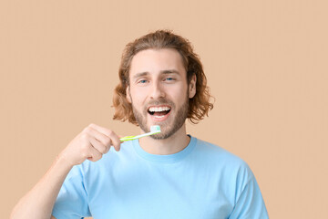 Poster - Young man brushing teeth on beige background, closeup