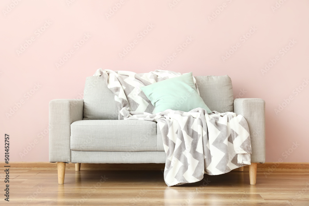 Modern sofa with pillow and plaid near color wall in room