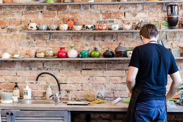 Wall Mural - A master in a pottery shop stands against a brick wall with shelves lined with pottery.