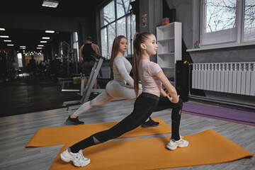 Lovely teenage girl warming up before workout with her personal trainer at the gym