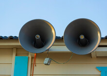 Pair Of Big Retro Loudspeakers The Roof Outside Against Blue Sky. Urgent Or Emergency Announcement Concept. Closeup The Speaker Mounted. The Public Voice Warning System Is Installed On The Building.