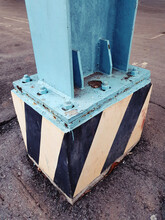 Closeup Shot Of Blue Metal Pillar Fastened To Cement Block With Anchor Bolts And Nuts During Daytime