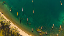 Aerial Top View Of Small Wooden Boats On A Green Body Of Water Near The Shore In The Sunlight