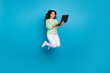 Full size photo of cute mature brunette lady jump hold laptop wear shirt pants shoes isolated on blue background