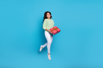 Wall Mural - Full body photo of impressed young brunette lady jump hold present wear shirt pants footwear isolated on blue background