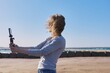© Valerii Honcharuk - Middle-aged woman recording video on smartphone with outdoor on seashore