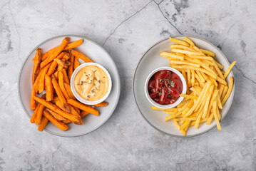 Two plates full of sweet potato fries and French fries with sauces, top view