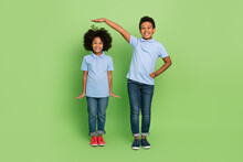 Full Length Body Size View Of Two Attractive Trendy Cheerful Pre-teen Kids Measuring Growth Isolated Over Green Color Background