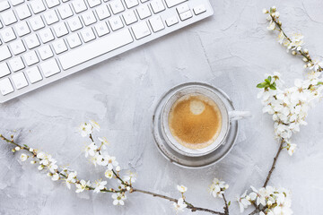 Computer keyboard on spring gray background with white cherry blossom flowers and morning espresso coffee cup. Studying, distance learning, freelance, lifestyle, internet shopping concept. Spring mood