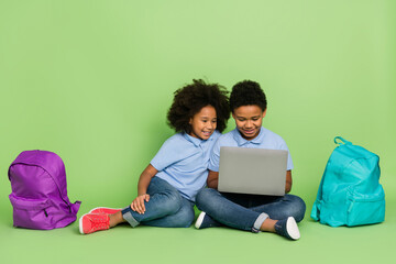 Portrait of attractive cheery pre-teen trendy friends friendship sitting using computer web website media isolated on green color background