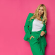© studioloco - Beautiful blond woman in unbuttoned green jacket and pantsuit is posing with hand in pocket.