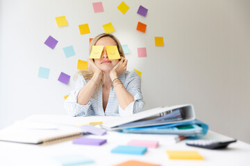Wall Mural - Business woman sits behind her desk on which are many office things and has sticky notes with drawn eyes on her face and sleeps