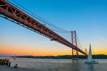 Lisbon, Portugal - November 14 2022 - Bridge Of April 25th (Ponte 25 De Abril) Crossing The Duoro River With In Front A Sailing Boat