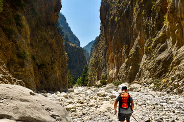 man with orange backpack hiking in mountain valley by hot summertime in samaria gorge in greece