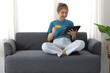 © Wasan - Cheerful Asian young woman lifestyle while sitting on sofa at home using tablet and having fun. Woman holding credit card and shopping online.