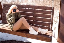 Blond Woman Takes A Picture On Digital Photo Camera Canon Sitting On Branch In Sunny Winter Day